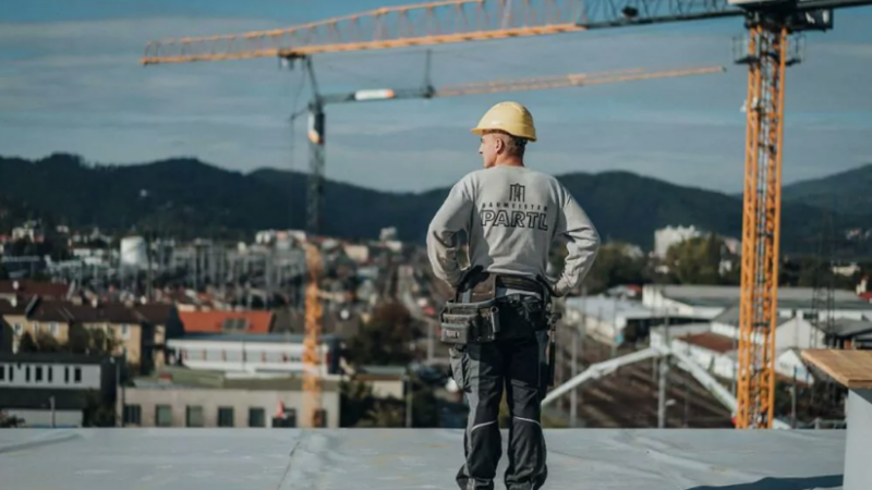 Mitarbeiter von Partl Bau steht am Dach einer Baustelle und stemmt seine Hände in die Hüfte. Dahinter steht ein großer Kran von Parl Bau