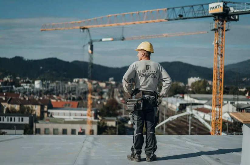 Mitarbeiter von Partl Bau steht am Dach einer Baustelle und stemmt seine Hände in die Hüfte. Dahinter steht ein großer Kran von Parl Bau