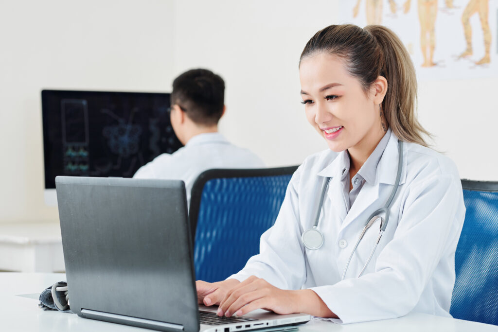 Junge Medizinerin die vor einem PC sitzt