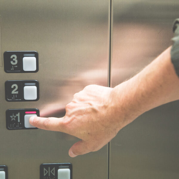 Hand drückt auf einen Knopf bei einem Aufzug