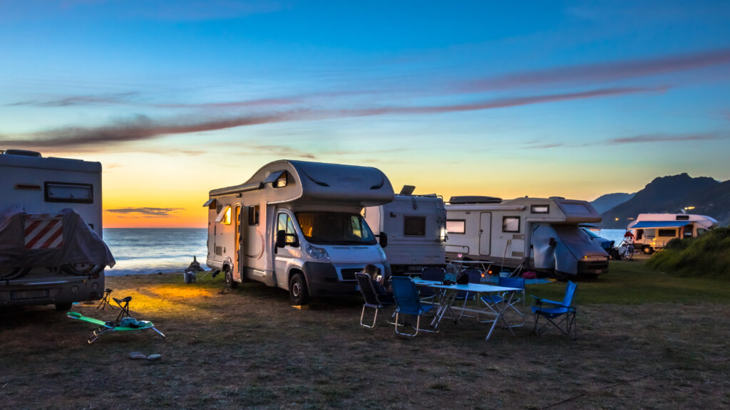 Sonnenuntergang am Meer. Davo stehen mehrere Wohnmobils und auch Outdoormöbel zum Sitzen. 