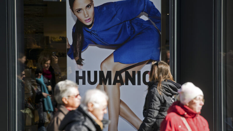Ansicht eines HUMANIC-Plakates in einem Schaufenster. Menschen gehen daran vorbei.