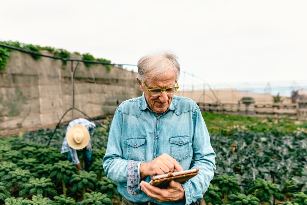 Älterer Herr mit einem Tablet in der Hand der auf in einen Anbaugebiet steht