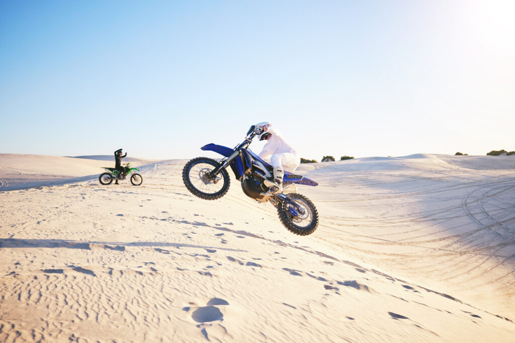 Wüste und zwei Motorradfahrer. Einer davon macht einen Luftsprung mit seinem Motorrad