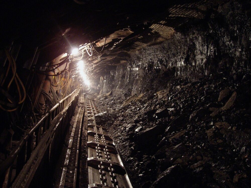 Ein Minenschacht mit Stützbalken und warmem Licht symbolisiert die Bergbautätigkeit von Pan African Resources – Foto: hangela / Pixabay