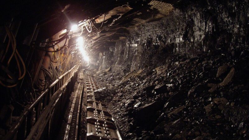 Ein Minenschacht mit Stützbalken und warmem Licht symbolisiert die Bergbautätigkeit von Pan African Resources – Foto: hangela / Pixabay
